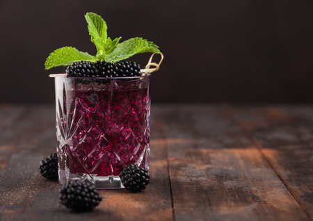 Glass of summer cocktail with blackberry with ice cubes and mint on wooden background with berries. Soda and alcohol mix.Space for textの写真素材