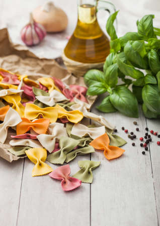 Farfalle pasta in brown paper on light wooden table background with basil and garlic and onion....