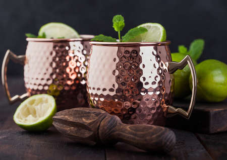 Moscow mule cocktail in a copper mug with lime and mint and wooden squeezer on dark kitchen background.の写真素材