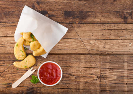 Buttered chicken nuggets in paper bag with wooden forks and ketchup on wood background.の写真素材