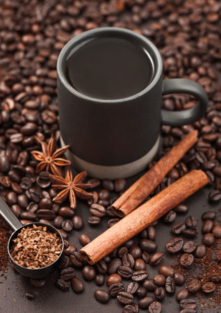 Black coffee in tall cup with anise star and cinnamon on ground coffee and beans background with coffee scoop.の写真素材