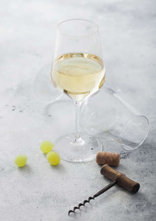 Glass of white homemade wine with corks, corkscrew and grapes on light stone background with empty glass.の写真素材