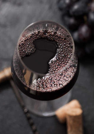 Glass of red wine with corks and vintage corkscrew on dark with grapes. Top view