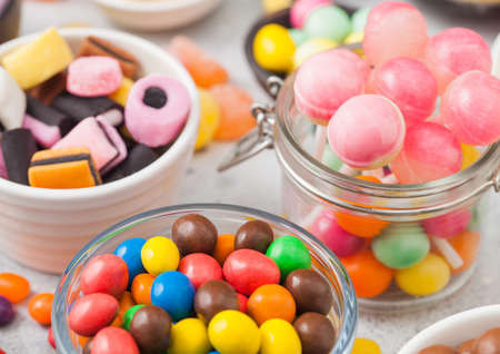 Pink lollipop candies in jar with various milk chocolate on white table background with liquorice allsortsの写真素材