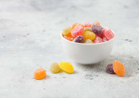 Various color and taste jelly sweet sugar candies in ceramic bowl on light table background.