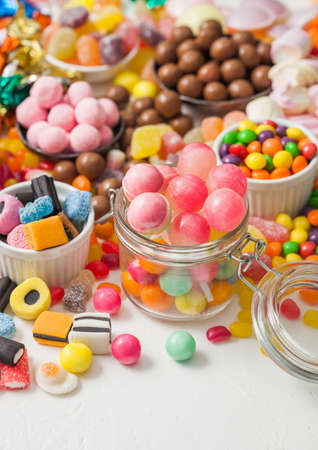 Pink lollipop candies in jar with various milk chocolate and jelly gums candies on white with liquorice allsorts and strawberry bonbonsの写真素材