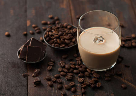 Glass of Irish cream baileys liqueur with coffee beans and dark chocolate in steel bowl on dark wood...