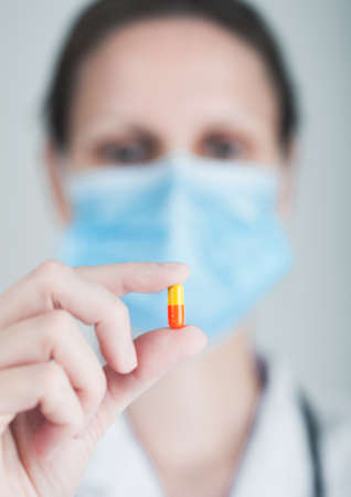 Doctor wearing blue face medical mask holding tablet pill on grey hospital wall background. Antibiotics and virus treatment tablet.の写真素材