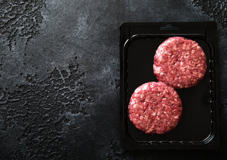 Raw minced beef burgers in plastic vacuum tray on black stone background.Top viewの写真素材