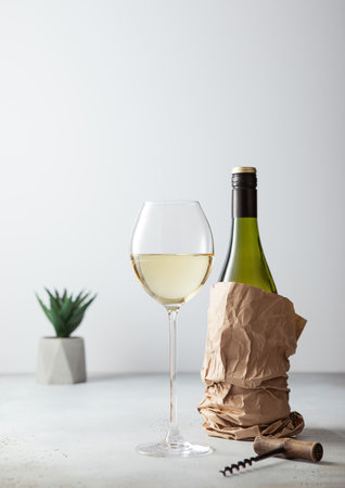 Bottle of white wine in paper bag with opener and glass of wine on light board.の写真素材