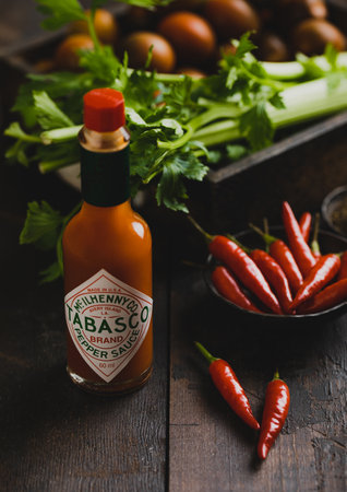 LONDON, UK - MARCH 22, 2023: Tabasco red pepper sauce bottle on wooden background with red peppers and celery.Top view.のeditorial素材