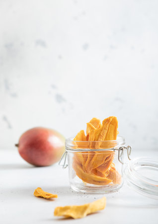 Dried mango pieces in glass jar and raw fruit on light background.Macroの写真素材