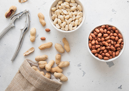 Whole and peeled peanut nuts with cracker and linen bag on light background.