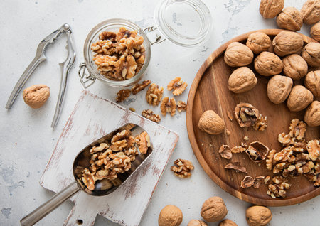 Wooden plate with whole and peeled walnut nuts with scoop and cracker on light background.の写真素材