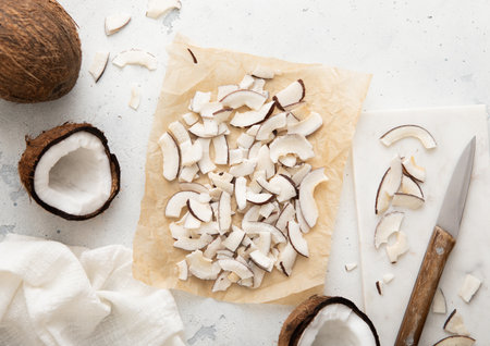 Organic sweet coconut slices chips on in baking tray with knife and ripe coconuts on light table.Top...