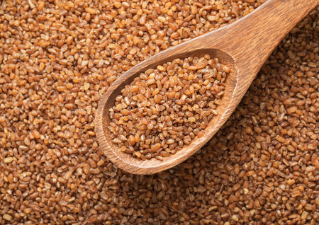 Spoon with raw organic healthy brown bulgur seeds.