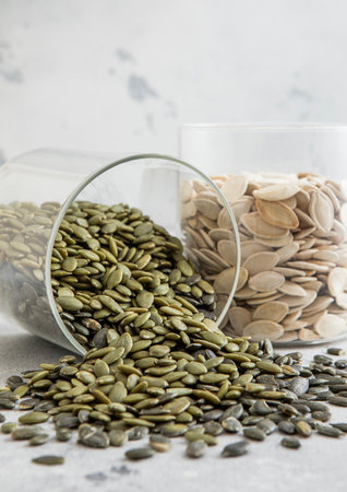 Glass jars with healthy raw pumpkin seeds whole and peeled on white kitchen table.の写真素材