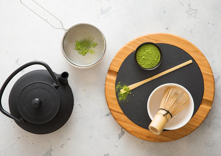 Japanese iron kettle with matcha green tea powder with whisk and spoon and bowl with sifter on white...