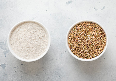 Bowls plates with green dry raw buckwheat seeds and flour powder on kitchen table.の写真素材