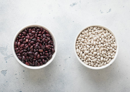 Ceramic bowls with white and red raw dry beans on kitchen table.