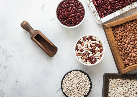 Dry raw white red and mixed beans in ceramic bowls and wooden boxes on light table.