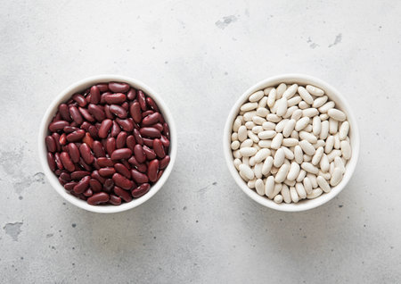 Ceramic bowls with white and red raw dry beans on kitchen table.
