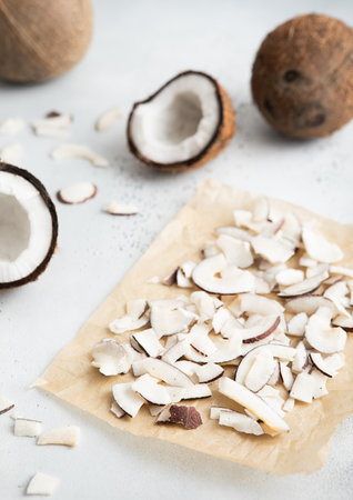 Dried organic coconut slices chips on baking paper with whole ripe coconut on light background.の写真素材