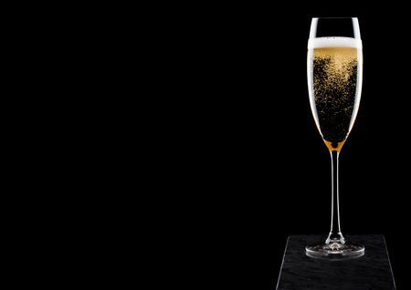 Elegant glass of yellow champagne with bubbles on black marble board on black background.の写真素材