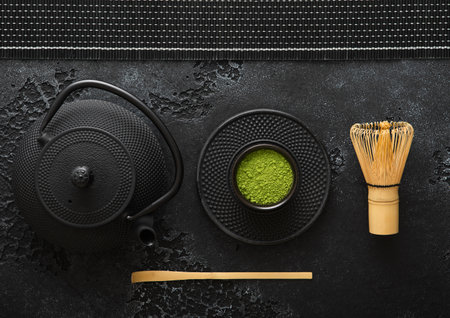 Organic matcha green tea powder with bamboo whisk and spoon and japanese traditional iron cast kettle on black background.の写真素材