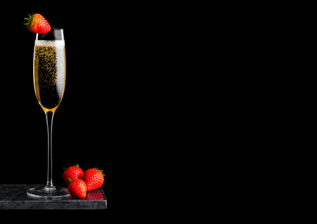 Elegant glass of yellow champagne with strawberry on top and fresh berries on black marble board on black.の写真素材