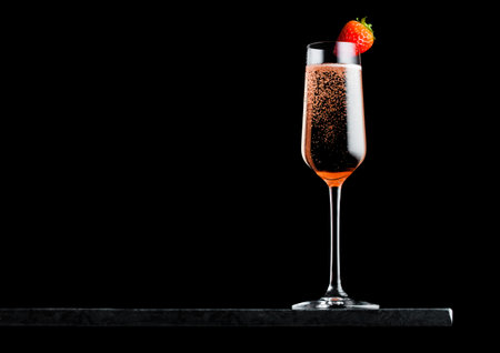 Elegant glass of pink rose champagne with strawberry on top on black marble board on black background.の写真素材