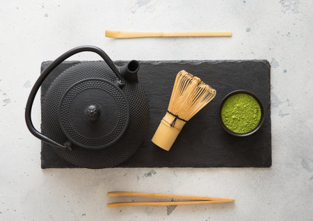 Green matcha tea powder with whisk and and spoon with iron kettle on stone board on white background.の写真素材