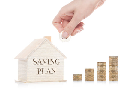 Wooden house model with coins next to it and hand holding the coin with conceptual text. Saving Planの写真素材