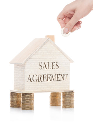 Wooden house model standing on coins and hand holding the coin with conceptual text.  Sales Agreementの写真素材