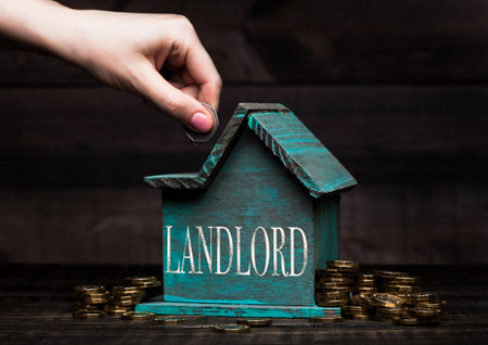 Wooden house model with coins next to it and hand holding the coin with conceptual text. Landlordの写真素材
