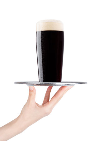 Hand holds tray with cold stout dark beer with dew on white background with reflectionの写真素材
