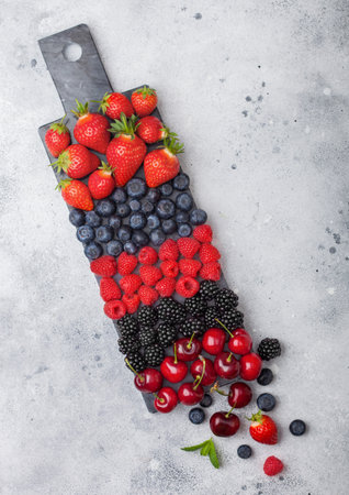 Fresh organic summer berries mix on black marble board on light kitchen table background. Raspberries, strawberries, blueberries, blackberries and cherries. Top viewの写真素材