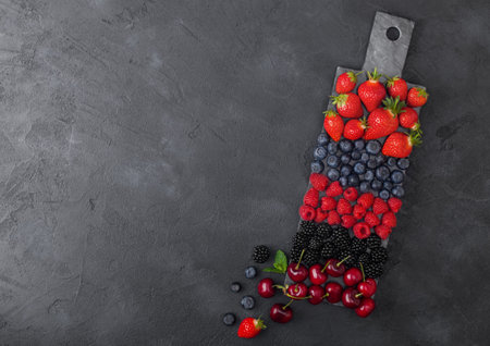Fresh organic summer berries mix on black marble board on dark kitchen table background. Raspberries, strawberries, blueberries, blackberries and cherries. Top viewの写真素材