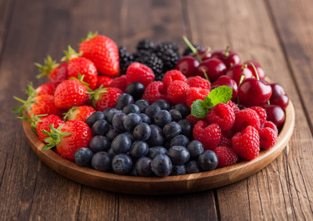 Fresh organic summer berries mix in round wooden tray on light wooden table background. Raspberries, strawberries, blueberries, blackberries and cherries. Top viewの写真素材