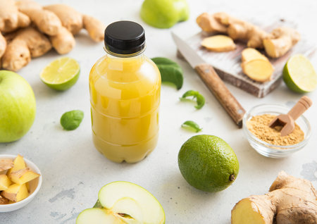 Bottle of energy shot immune drink with ginger and green apples with limes on light background.の写真素材