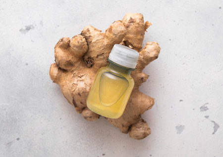 Bottle of immune ginger energy shot drink on top of fresh raw ginger root to light background.の写真素材