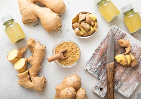 Immune ginger energy shot drink bottles with fresh raw ginger root and powder on light background.の写真素材