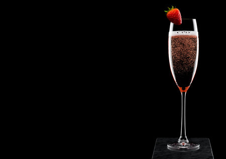 Elegant glass of pink rose champagne with strawberry on top on black marble board on black background.の写真素材