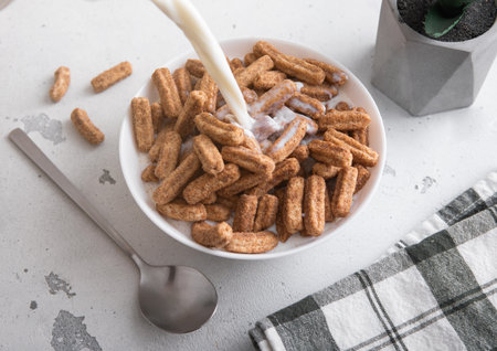 Sweet churros breakfast cereal in plate and pouring milk into it with spoon on table.の写真素材