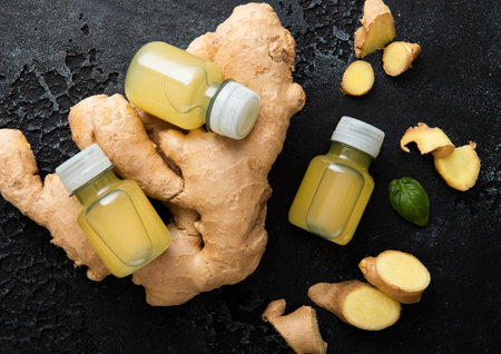 Bottles of immune ginger energy shot drink with ginger roots on black background.の写真素材