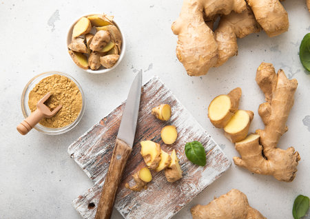 Raw fresh ginger root slices chopped with knife on wooden board with ginger powder on background.の写真素材