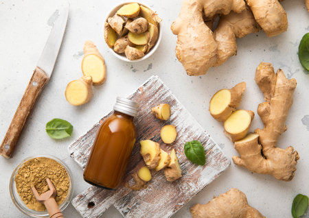 Raw fresh ginger root slices chopped with knife on wooden board with immune energy drink on background.の写真素材