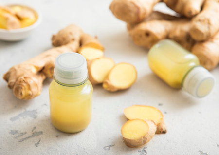 Immune ginger energy shot drink bottles with fresh raw ginger root on light background.の写真素材