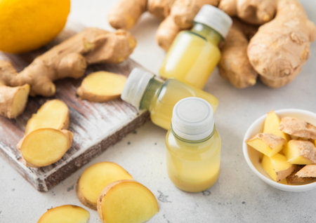 Immune ginger energy shot drink bottles with fresh raw ginger root and lemon on light background.の写真素材