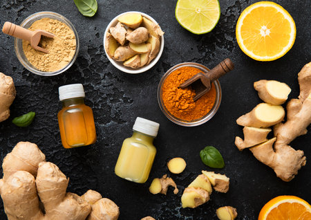 Bottles of immune turmeric ginger energy shot drink with fresh raw ginger roots and oranges fruits on black background.の写真素材